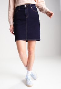 Marinblå denimkjol med rak skärning, sidofickor och kontrasterande gula sömmar. Kombinerad med lätta sneakers och vita strumpor.