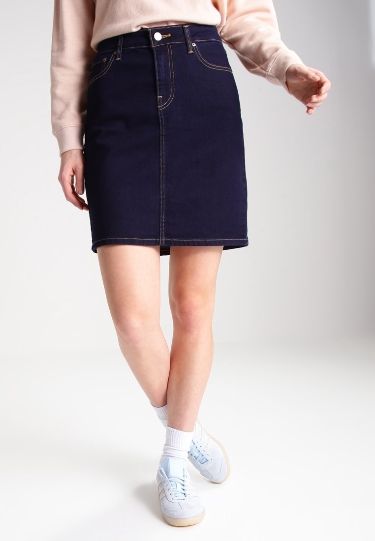 Marinblå denimkjol med rak skärning, sidofickor och kontrasterande gula sömmar. Kombinerad med lätta sneakers och vita strumpor.