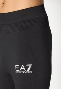 Juodos sportinės legging'os su tekstūruotu liemeniu ir šoniniu logotipu, pasižyminčios prigludusia forma ir minkšta medžiaga komfortui.