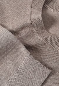 Gros plan d’un pull en maille beige plié montrant les détails du col et des poignets côtelés avec un tissu doux et texturé.