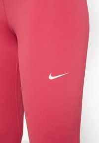 Leggings sportivi rosa realizzati in materiale elastico, con un piccolo logo Nike bianco sulla coscia e dettagli delle cuciture piatte.