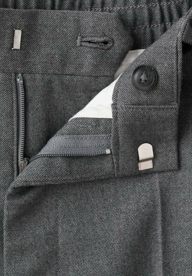 Graue, strukturierte Hose mit einem Reißverschluss, Knopf, metallischen Akzenten und einem elastischen Bund mit Kordelzug. Innenfutter mit weißem Futter.