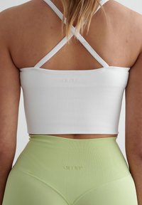 Un crop top blanc à côtes avec des bretelles croisées, associé à un legging à côtes léger vert clair taille haute avec un détail de logo.