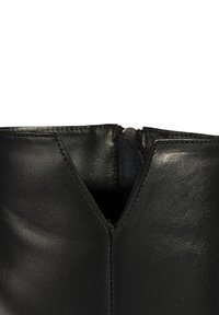 Nahaufnahme des oberen Teils eines schwarzen Lederstiefels mit einem V-förmigen Ausschnitt und sichtbarem Reißverschluss im Inneren der Öffnung.