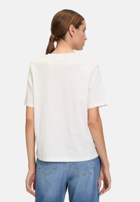 Hvid T-shirt med korte ærmer, afslappet pasform, rund halsudskæring og glat bomuldsstruktur, parret med lyseblå denimjeans.