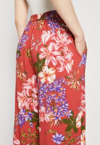 Rode bloemenbroek met een brede pijp, voorzien van witte en paarse bloemen, een elastische tailleband en zijzakken. Zachte stof met een levendige print.