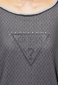 Débardeur en maille grise présentant un graphique triangulaire avec "Glen" et "3" imprimés en gris plus foncé. Design de vêtements de sport avec des détails de couture visibles.