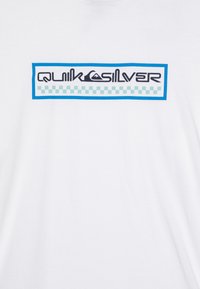 Bílý tričko s obdélníkovým logem modré, černé a tyrkysové barvy, na kterém je nápis "QUICKSILVER" a kostičkovaný vzor.