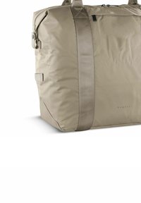 Borsa duffel in nylon beige con una superficie liscia, grande scomparto principale, zip superiore e robuste cinghie per il trasporto. Logo del brand visibile sul lato.