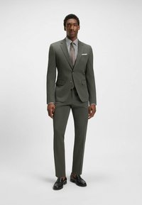 Dark green tailored suit with a textured finish, paired with a striped shirt and brown tie. Black loafers complete the outfit.