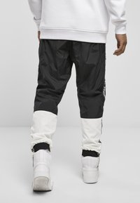 Svarta och vita trackbyxor med en glänsande yta, som har elastiska mudd och kontrasterande tygpaneler. Styla med vita höga sneakers.