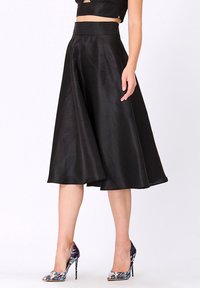 Une jupe A-line en satin noir à taille haute, arborant une texture lisse et une silhouette fluide, assortie à des talons hauts multicolores.