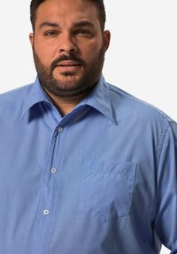 Lichtblauw overhemd met knopen gemaakt van geweven stof. Heeft een puntige kraag, enkele borstzak en een subtiele textuur over het hele shirt.