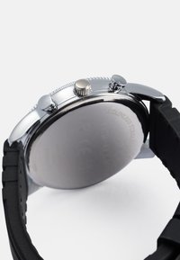 Orologio in acciaio inox argento con cinturino in gomma nera. Presenta tre pulsanti, una corona testurizzata e un fondello lucido.