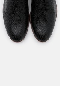 Chaussures habillées en cuir noir avec un motif écaille texturé, présentant un design classique à lacets et une semelle brun contrastante.