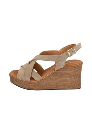 Sandalia cuña beige de ante con tiras cruzadas, puntera abierta, tira en el tobillo y hebilla dorada sobre una plataforma con textura de madera marrón.