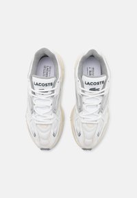 LACOSTE-sneaker i hvitt og grått mesh med teksturerte overlegg, grå fòr, og en kremfarget gummisåle; har snøring og merkevare.