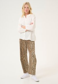 White, button-up shirt with textured fabric and embroidered details on sleeves; paired with leopard print, wide-leg pants and white sneakers.