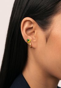Pendiente de aro dorado y pendiente de tuerca en forma de caracol verde en la oreja de un modelo, mostrando superficies brillantes y colores vibrantes contra el cabello oscuro.