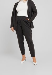 Ciemnoszary, lekki kardigan z długim rękawem na białym, prążkowanym golfie, zestawiony z ciemnoszarymi, zwężającymi się spodniami i białymi szpilkami.