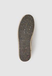 Suela de un zapato con un caucho negro texturizado y motas multicolores, bordeada por un material tejido beige claro.