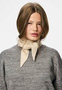 Bufanda beige atada alrededor del cuello de una persona que lleva un suéter de punto gris. Textura suave con un diseño sencillo y patrones sutiles.
