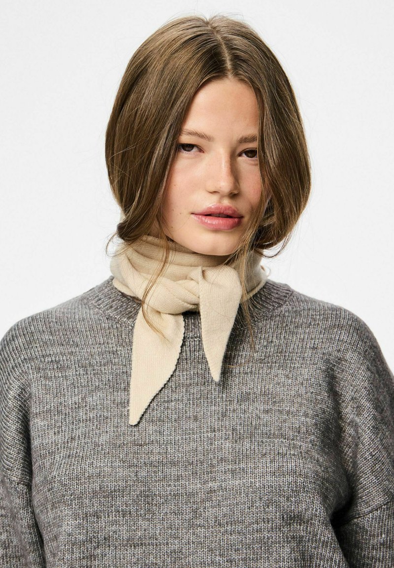 Bufanda beige atada alrededor del cuello de una persona que lleva un suéter de punto gris. Textura suave con un diseño sencillo y patrones sutiles.