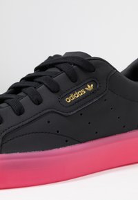 Black leather sneaker with black laces, perforated detailing, gold "adidas" logo, and a pink translucent sole.