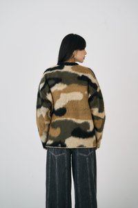 Camo-mønstret strikkegenser i beige, grønn og svart, med avslappet passform, myk tekstur og ribbestrikket hals. Kombinert med vide svarte jeans.