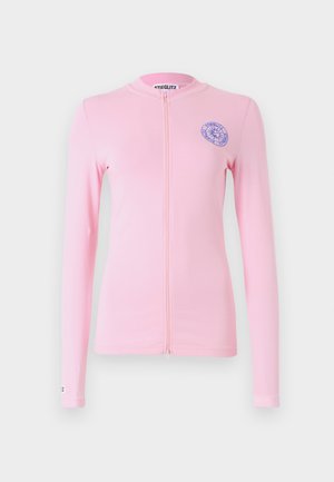 Jasnoróżowa bluzka z długim rękawem na zamek błyskawiczny, z okrągłym dekoltem i haftowanym niebieskim logo po lewej stronie klatki piersiowej. Gładki materiał i dopasowany fason.