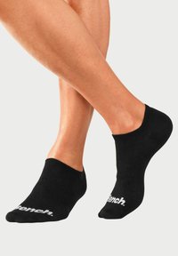 Schwarze Knöchelsocken mit gerippter Textur und weißem Logo. Niedrig geschnittenes Design, eng anliegend am Knöchel, geeignet für Freizeitkleidung oder Sport.