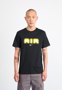 Svart bomull t-skjorte med en bare, gult utstikkende "AIR" grafikk og en liten hvit Nike-logo på brystet. Korte ermer og rund hals.