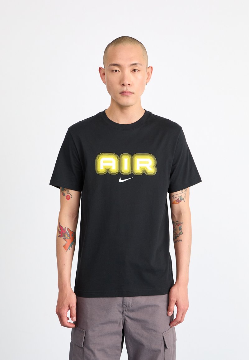 Juodas medvilninis marškinėliai su ryškiu geltonu "AIR" piešiniu ir mažu baltu Nike logotipu ant krūtinės. Trumpomis rankovėmis ir apvalia kaklo iškirpte.