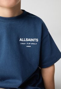 Granatowy bawełniany t-shirt z białym logo "ALLSAINTS", dodatkowym tekstem w języku japońskim oraz napisem "LONDON" poniżej. Krótkie rękawy, okrągły dekolt.
