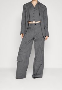 Szary, dopasowany garnitur z krótką kamizelką i szerokimi spodniami cargo. Tkanina ma subtelny wzór w paski oraz wiele kieszeni.