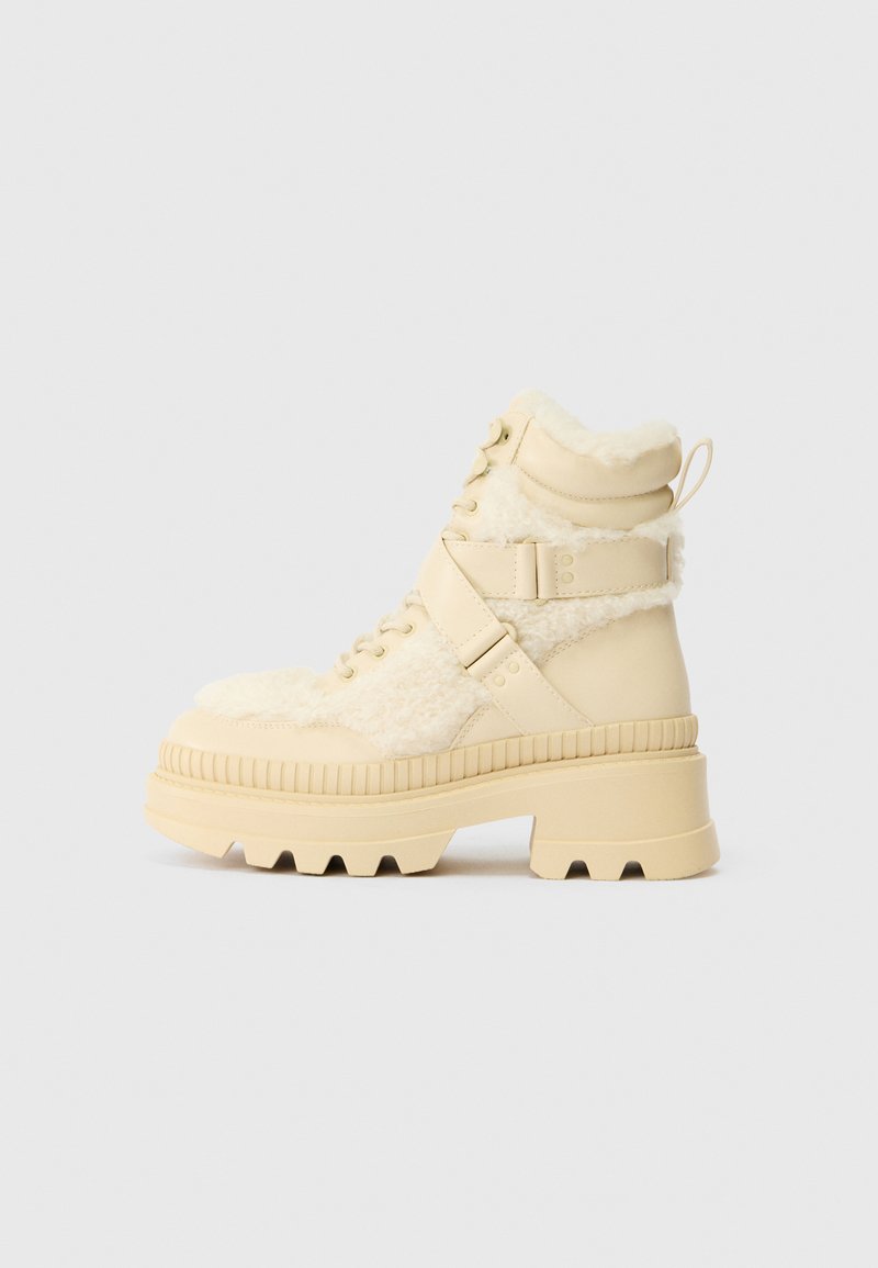 Stivali alla caviglia beige con una parte anteriore in shearling testurizzato e lati in pelle liscia. Suola in gomma spessa con scanalature profonde e cinghie regolabili.