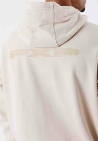 Hoodie con cappuccio leggermente beige realizzato in morbido tessuto, dotato di cappuccio cucito e grande logo "PXP" in una tonalità leggermente più scura sul retro.