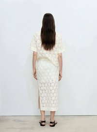 Weißes, blumenmusterndes Zweiteiler-Outfit mit einem kurzärmeligen Oberteil und einem knielangen Rock. Weicher, strukturierter Stoff mit seitlichem Schlitz und Sandalen.