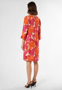Robe florale dans des teintes de rose et d'orange, manches trois-quarts, longueur genou, avec une fermeture à bouton au dos et une coupe cintrée.