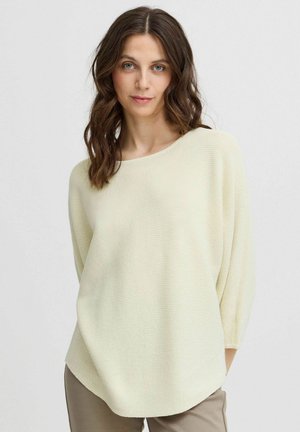 Pull léger jaune tricoté avec un large col bateau, des manches trois-quarts et un motif texturé en côtes, associé à un pantalon beige.