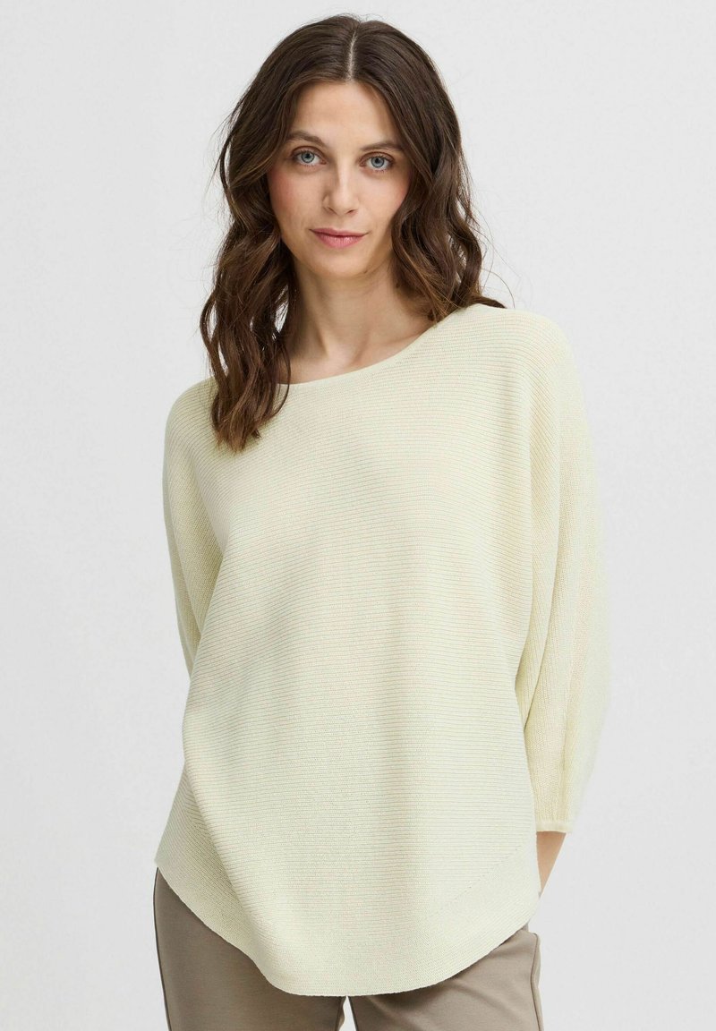 Helles gelbes Strickpullover mit weitem Bootsausschnitt, Dreiviertelärmeln und strukturiertem Rippenmuster, kombiniert mit beigen Hosen.