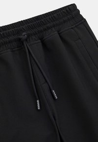 Sorte joggebukser med elastisk linning og snøring, sidelommer og metallaccenter med "GUESS" merkevare. Glatt tekstur.