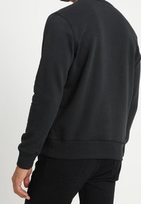 Sudadera negra con cuello redondo, mangas largas, puños y dobladillo de canalé, hecha de un tejido suave, con un diseño simple y sin adornos.