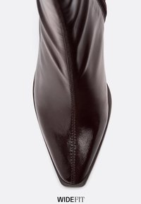 Burgundské kotníkové boty s špičatou špičkou, hladkým lakovaným koženým povrchem, bočním zipem a jemným prošíváním podél švů.