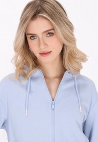 Felpa con zip di colore azzurro chiaro, dal tessuto morbido, con dettagli rosa a contrasto sui tirazip e un design dal taglio comodo.