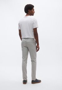 Ανδρικό ανοιχτό γκρι παντελόνι σε στενή γραμμή με ίσια φόδρα, τσέπες και διακριτή υφή, σε συνδυασμό με απλό λευκό t-shirt και σκούρα αθλητικά παπούτσια.