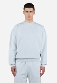 Lyseblå sweatshirt med ribbet rund hals og manchetter, og et lille, hvidt "PEGADOR" logo på brystet, lavet af blødt stof.