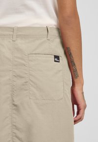 Shorts beige con una tasca posteriore con un piccolo etichetta nera. Il tessuto sembra morbido con una texture liscia e un design casual.