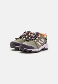 Green outdoor shoes with gray accents, textured mesh upper, rubber sole, and quick-lace system. Features orange interior and three white stripes.