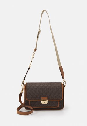 Sac bandoulière marron de créateur avec fermoir doré, bordure beige et bandoulière beige et marron réglable sur fond blanc.